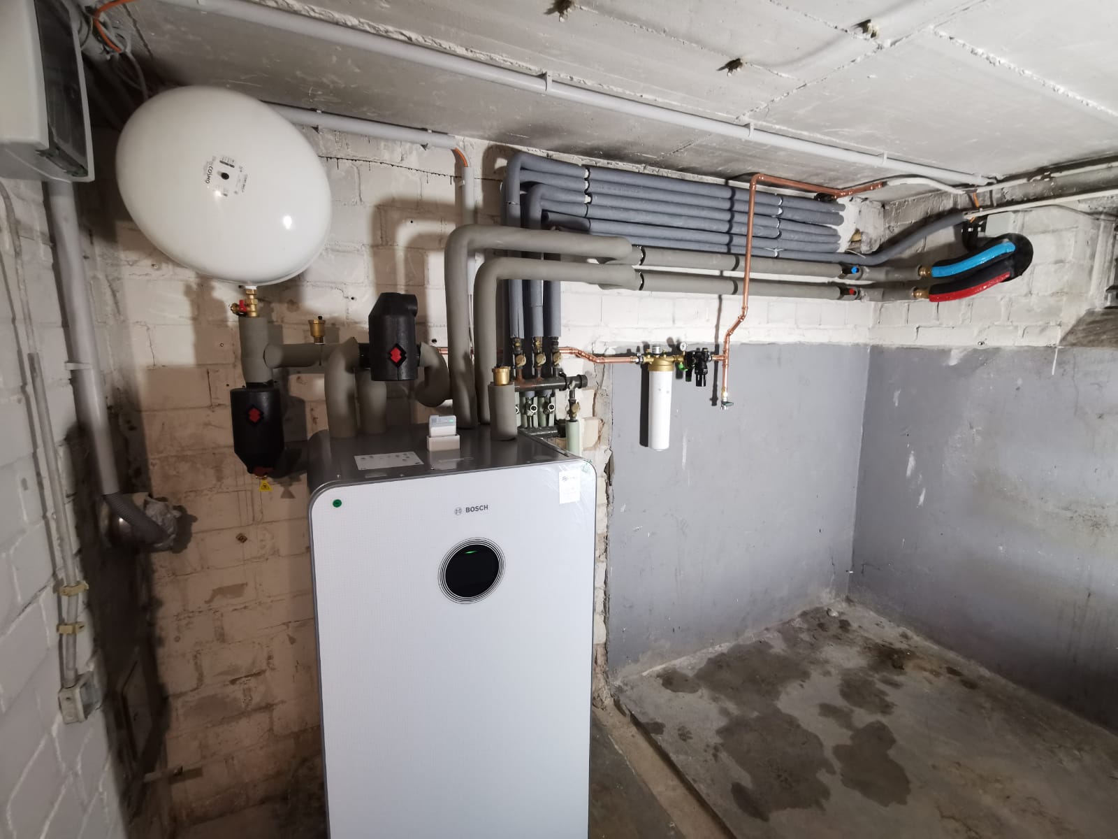 Bosch-Heizung im Keller mit isolierten Leitungen, Expansionsgefäß und freiliegender Ziegelwand.
